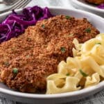 Breaded Pork Cutlets with buttered noodles and quick red cabbage sauerkraut on a dinner plate.