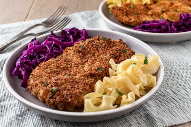 Breaded pork cutlet on plate with red cabbage and egg noodles.