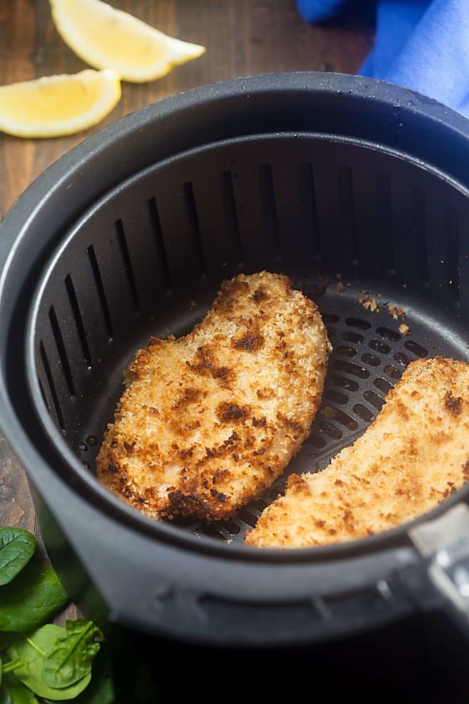 Two breaded chicken cutlets in the basket of an air fryer.