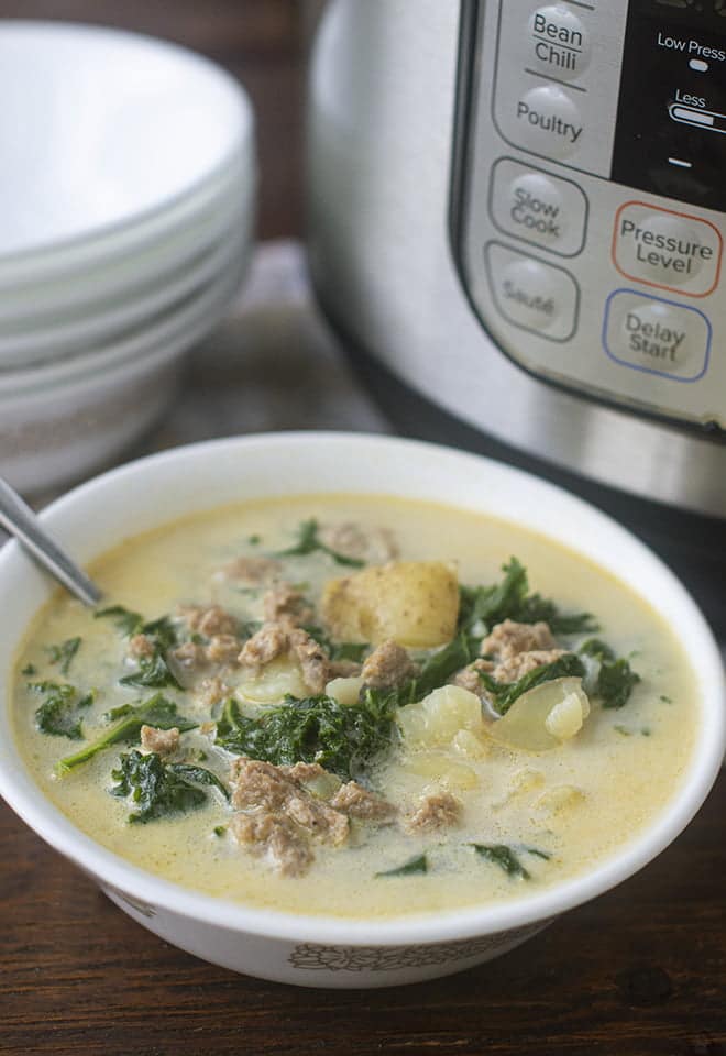 White bowl of Zuppa Toscana with sausage, kale, and potatoes.