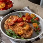 Breaded chicken cutlets topped to halved grape tomatoes in front of an air fryer.