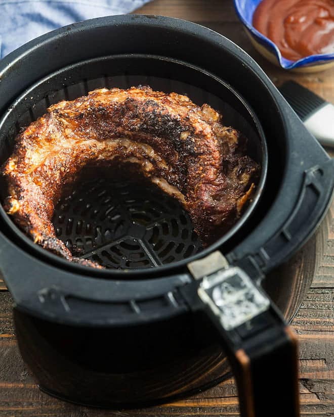 Pork ribs curled in the inside of an air fryer basket.