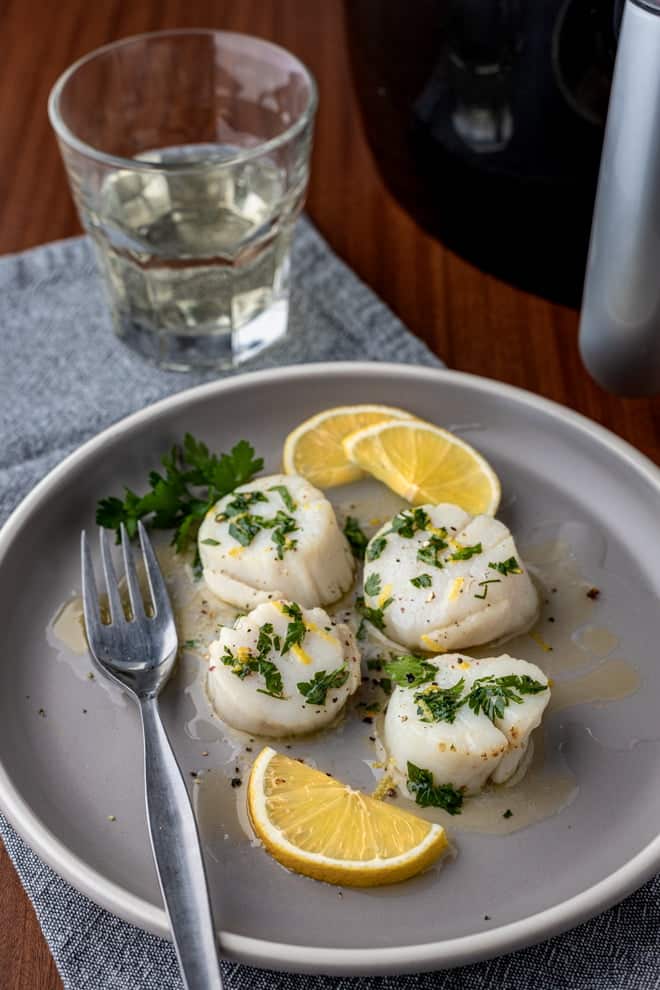 Scallops with lemon butter and parsley on a gray plate.