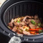 Slices of steak, bell pepper, and onion in air fryer basket.