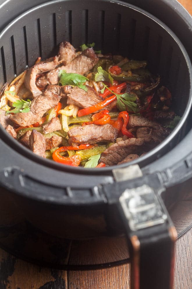 Strips of steak, bell pepper, and onion in an air fryer.