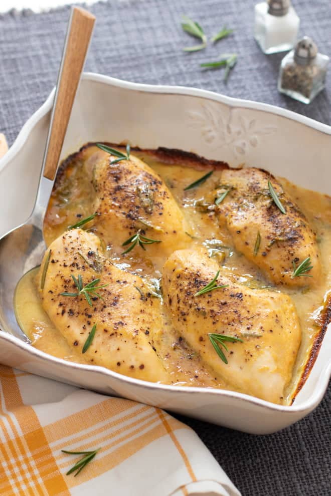 Honey Mustard chicken breasts topped with fresh rosemary, in a square white dish.