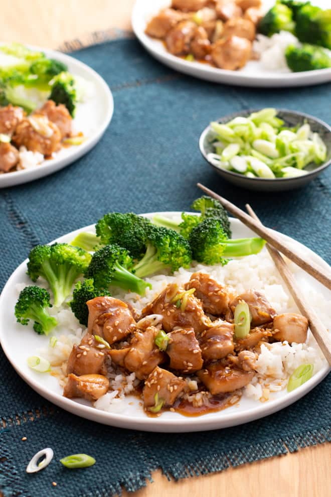 Teriyaki Chicken over rice with broccoli on the side, on a white plate with chopsticks.
