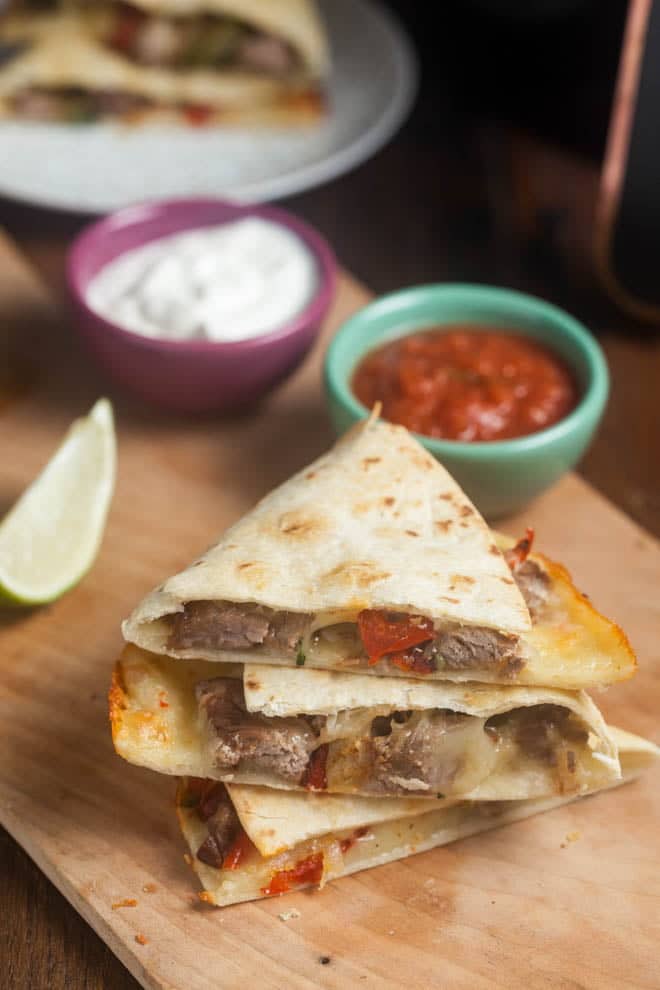 Steak Quesadillas cut in wedges, with bowls of salsa and sour cream.