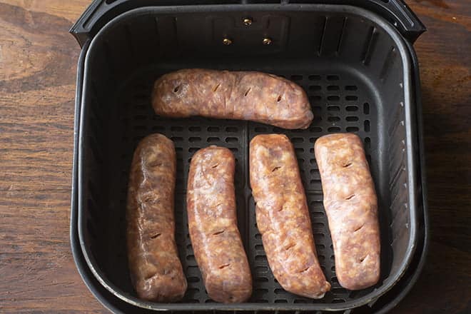 Raw sausages in air fryer basket, have been poked multiple times with paring knife.