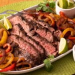 Grilled Fajita Dinner of steak strips surrounded by peppers and onions, with lime wedges on a white platter.