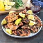 Grilled Chicken Thighs piled on a plate with lemon wedges.