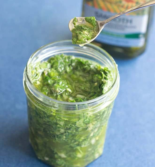 Salsa verde in glass jar with spoonful held above.