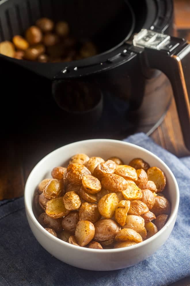Roasted baby potatoes in a white bowl in front of an Air Fryer.