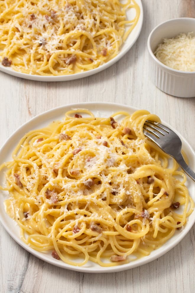 Spaghetti Carbonara topped with grated Parmesan on a white plate with a fork.