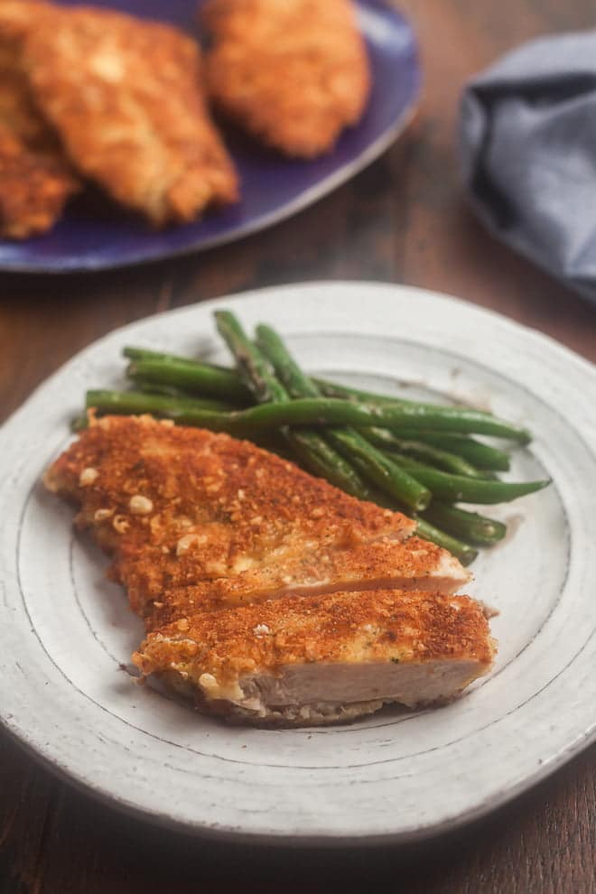 Crispy parmesan crusted chicken on a plate with green beans.