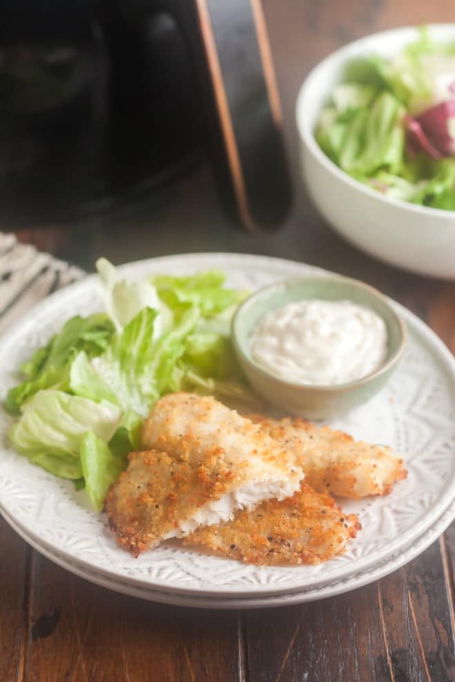 Crispy fish fillets on white plate with lettuce and tartar sauce.