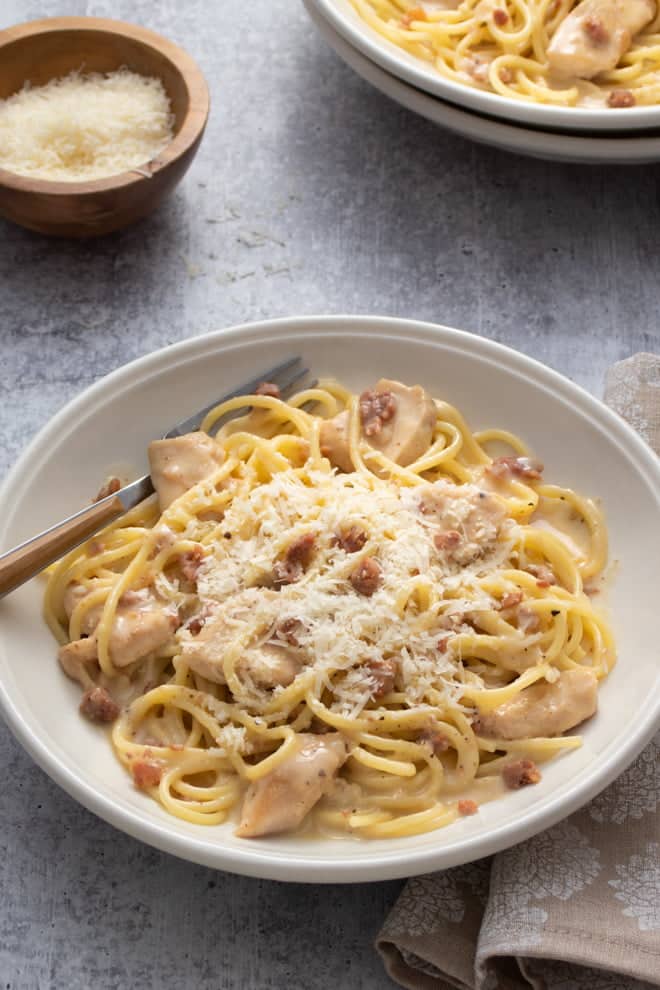 Chicken carbonara in a white low bowl topped with grated Parmesan.