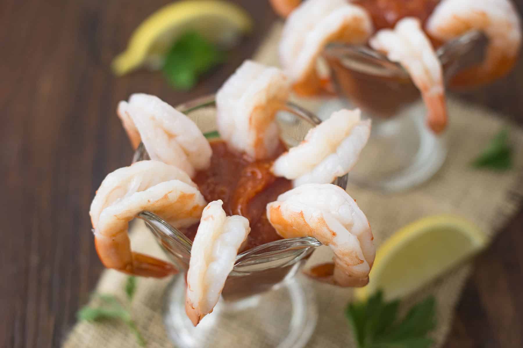6 shrimp hanging off of a glass with cocktail sauce in the glass.