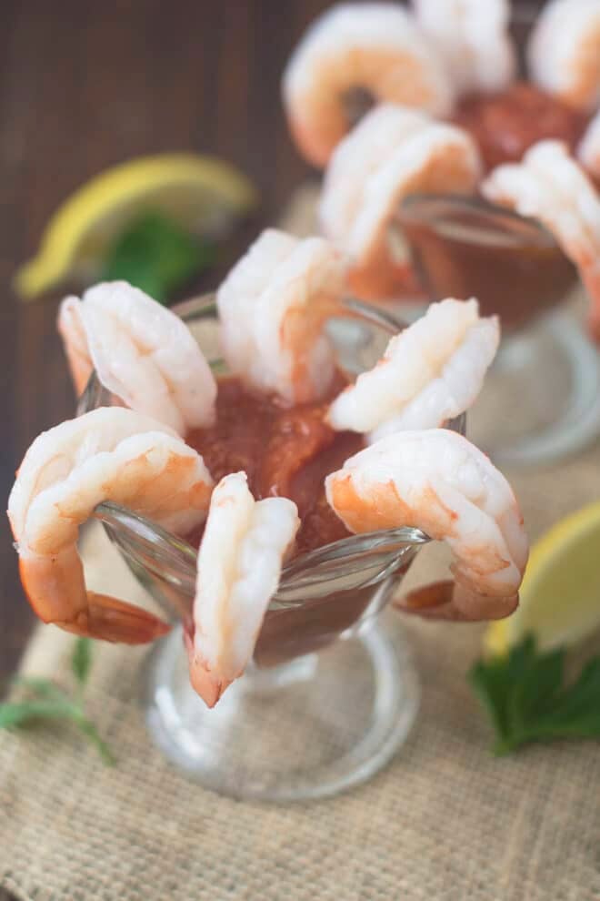 6 large shrimp dangling around a wine glass with cocktail sauce in the bottom of the glass