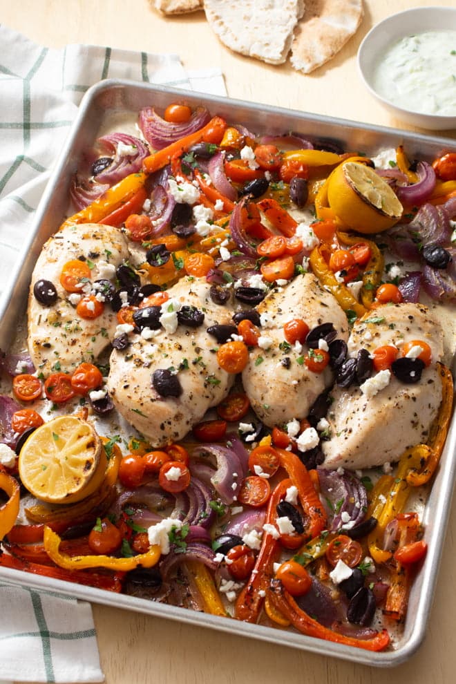 Greek Lemon Chicken on sheet pan with peppers, onion, tomatoes, and olives.