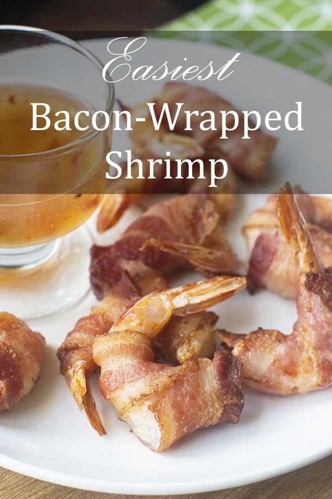 Shrimp wrapped in bacon on a white plate with a glass bowl full of sweet chili sauce. A green cloth in the background.