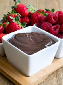 Creamy chocolate dip in white dish with bowls of strawberries and raspberries.