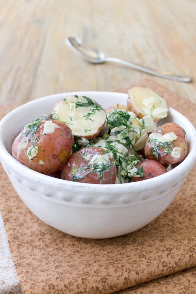 A white serving bowl full of red potatoes tossed with dill, cream, and sauteed onion.
