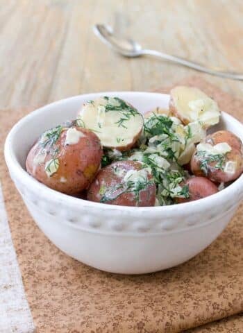 A white bowl full of halved red potatoes tossed with fresh dill, sauteed onions, and cream.