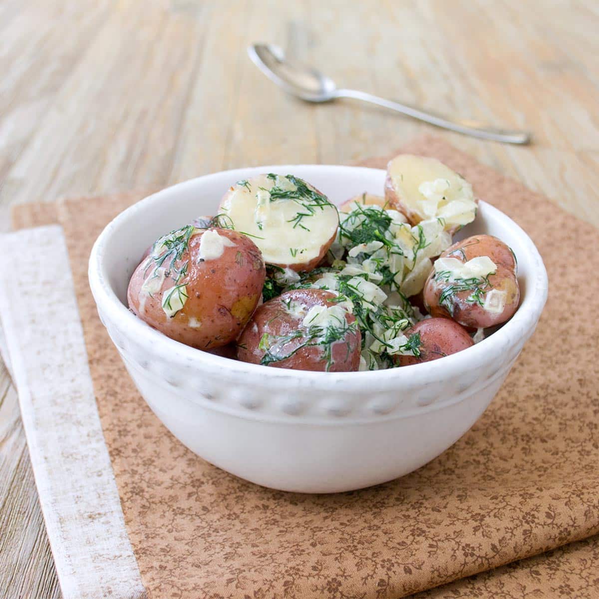 A white bowl full of halved red potatoes tossed with fresh dill, sauteed onions, and cream.