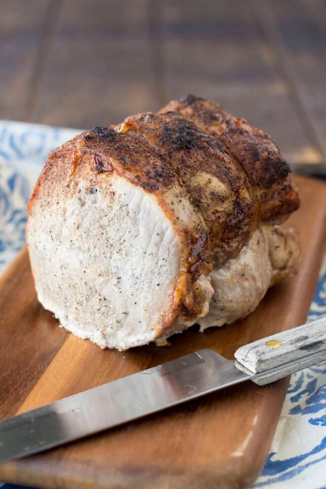 A pork loin roast tied with twine, golden brown crust, on a cutting board with a knife next to it.