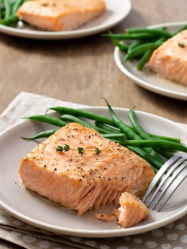 Flaky salmon fillet on a plate with green beans.