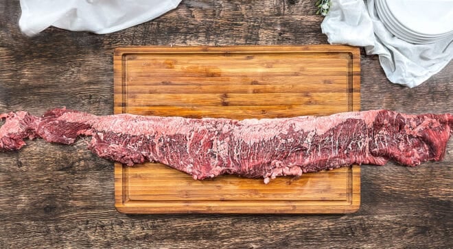 Full raw skirt steak over a wooden cutting board and counter.