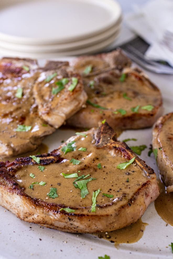 Bone-in pork chops covered in gravy and fresh herbs.
