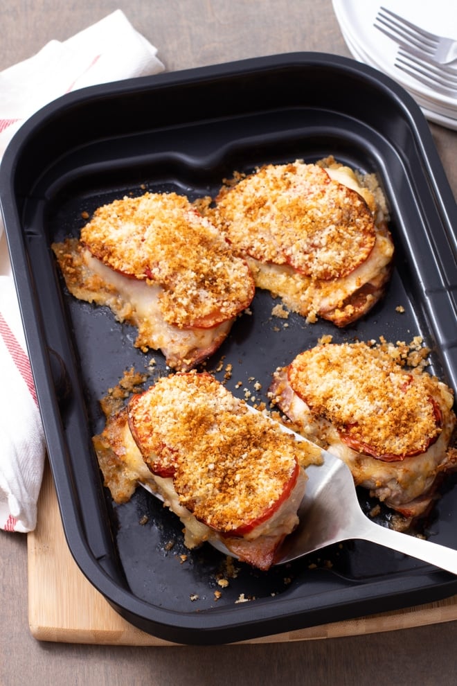 Chicken thighs topped with cheese, tomato, and bread crumb mixture in an air fryer tray.