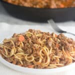 White plate of spaghetti with basic spaghetti sauce of tomatoes, ground meat, and veggies.