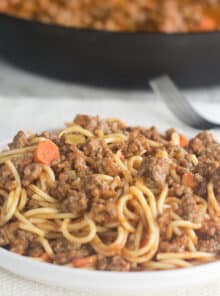White plate of spaghetti with basic spaghetti sauce of tomatoes, ground meat, and veggies.