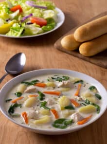 Chicken Gnocchi Soup with spinach and carrots in a creamy broth. Breadsticks and garden salad in background.