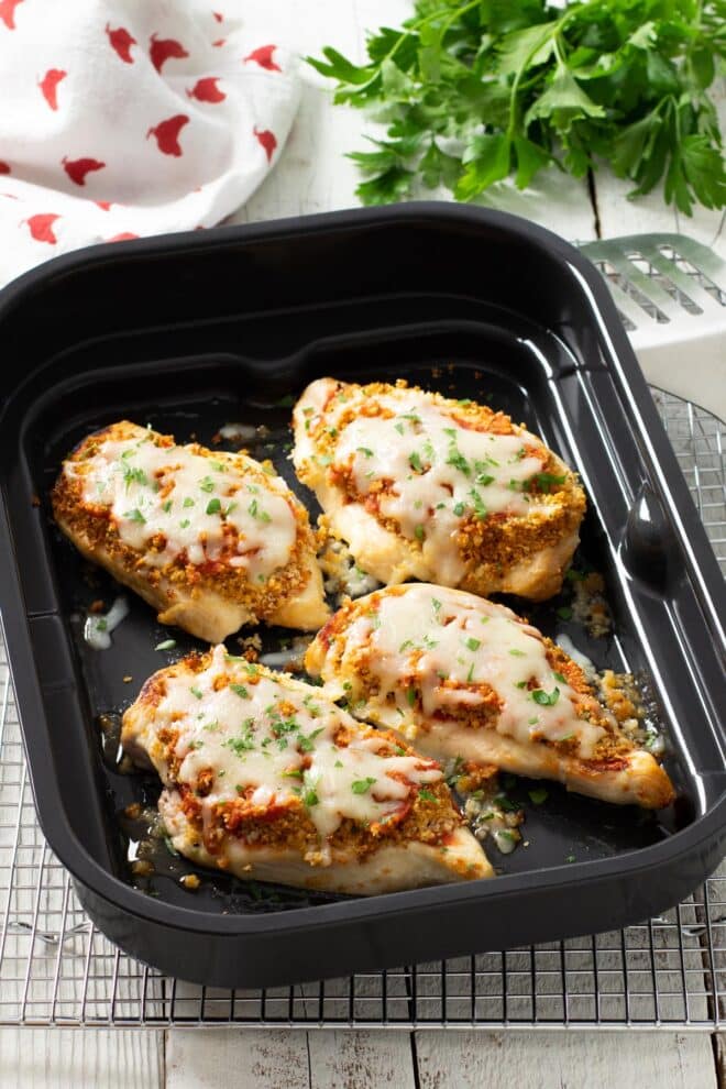 Four chicken breasts in an air fryer tray, topped with breadcrumbs, tomato sauce and melted mozzarella.