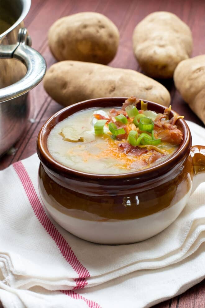Brown bowl of potato soup topped with cheese, green onion, and bacon.
