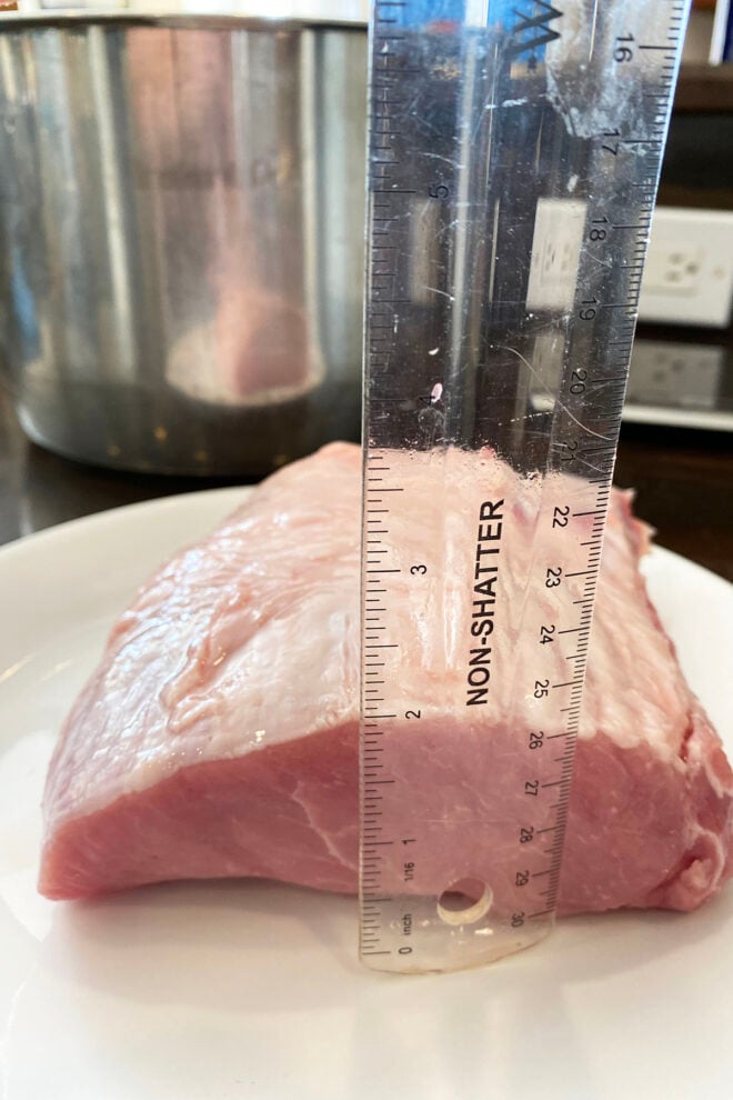 A raw pork loin on a plate with a clear ruler showing that it is 2 inches thick