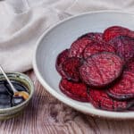 Grilled beet slices on a gray platter, with a small dish of balsamic glaze in the background.