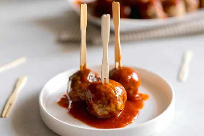 Three meatballs with wooden picks in them on a small white plate.