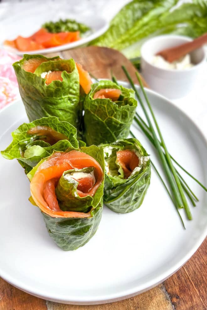 Lettuce rolls with smoked salmon and cream cheese on a white plate with chives.