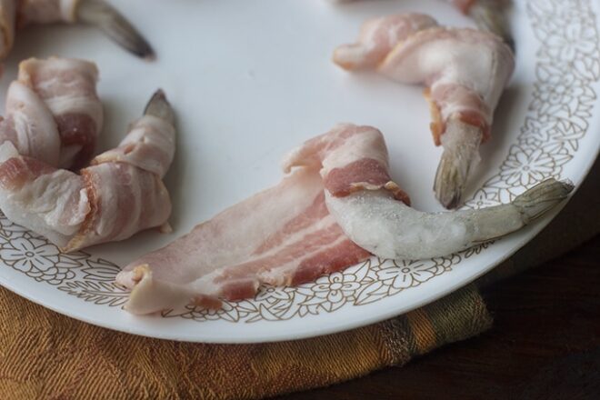 Frozen shrimp and raw bacon on a plate.