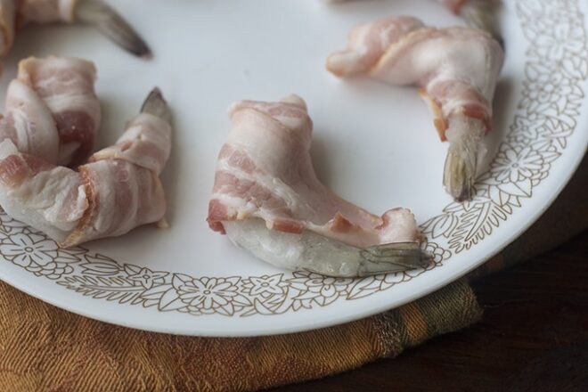 Bacon being wrapped around frozen shrimp.