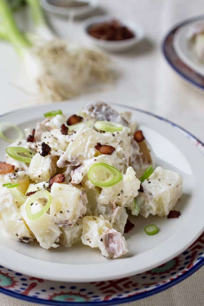 White plate with potato salad with bacon and green onions.