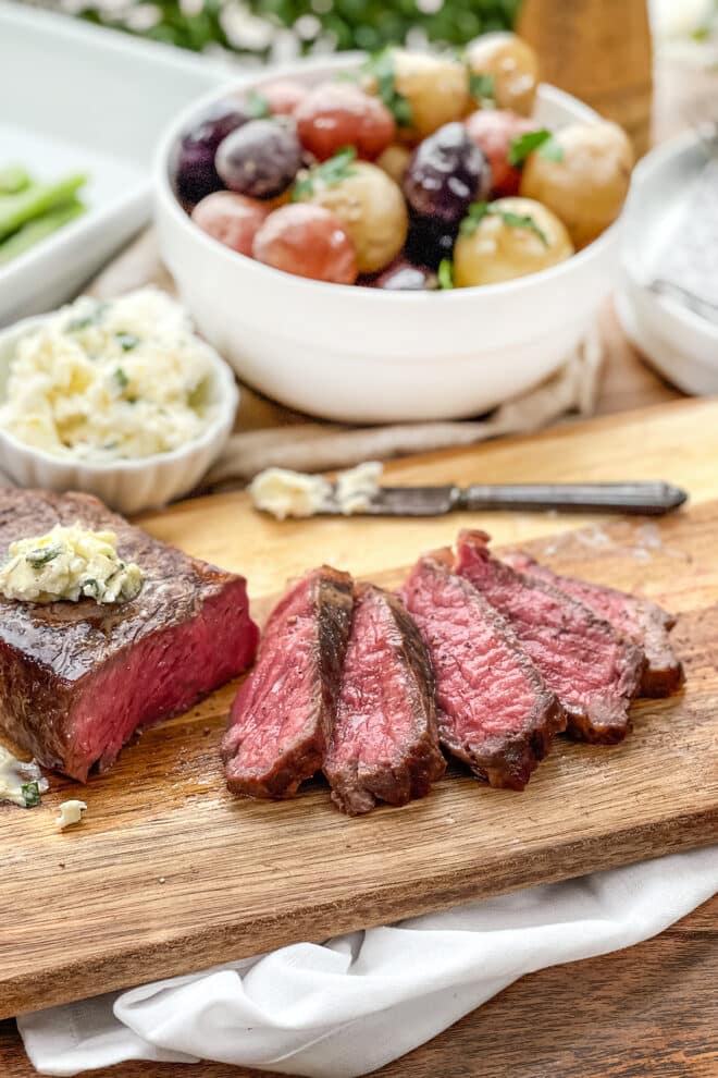 Strip steak with several slices cut on a wooden cutting board, topped with garlic butter.