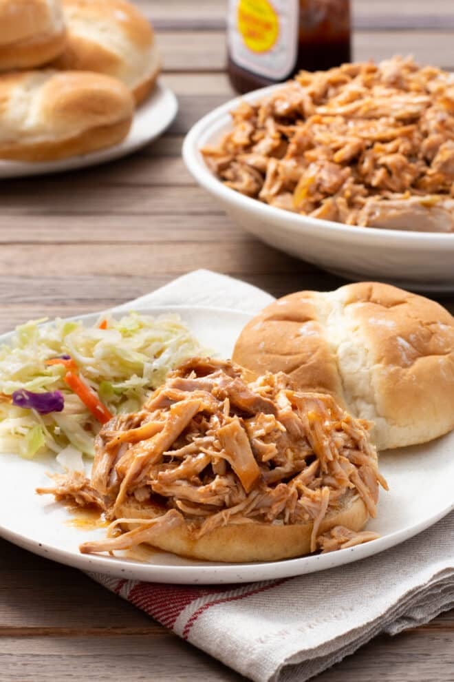 BBQ Pulled pork on a bun, with bun top and coleslaw on the white plate as well. 