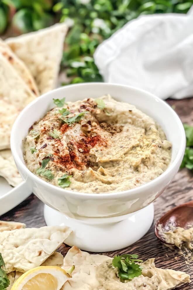 white dish of baba ganoush sprinkled with paprika and surrounded by pita wedges