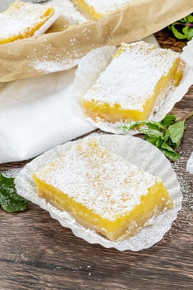 lemon bars dusted with powdered sugar set on white cupcake liners.